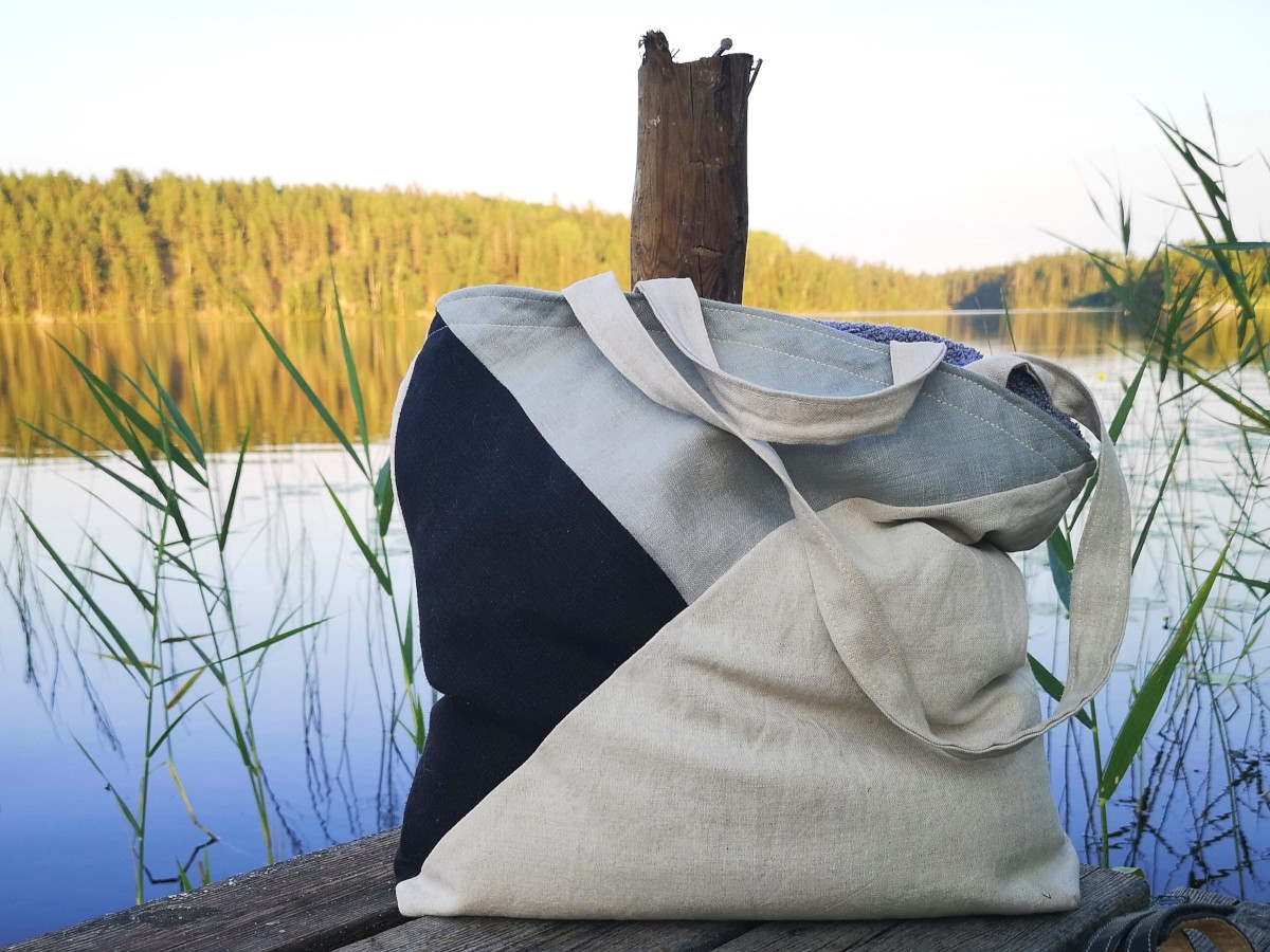 väska sytt på tygrester i färgerna beige, svart och ljusblå. Väskan står på en brygga vid en sjö i bakgrunden.
