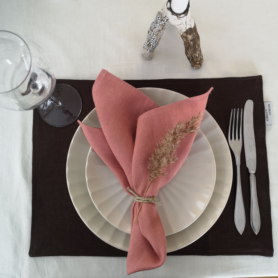 Brun bordstablett i linne dukat med porslin och bestick och rosa linneservett.