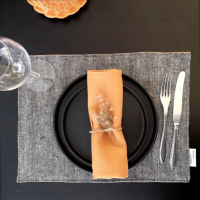 bordstablett i linne med fiskbensmönster dukat med porslin och bestick samt rostfärgad servett.