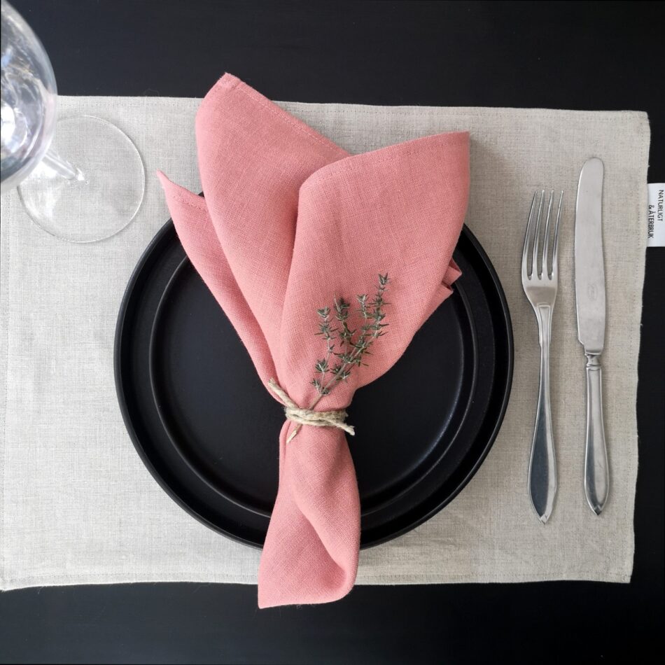 Naturfärgad bordstablett i linne dukat med porslin och bestick samt rosa servett.