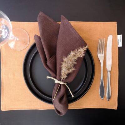 Rostfärgad bordstablett i linne dukat med porslin och bestick samt brun servett.