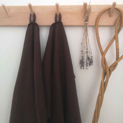 bruna handdukar i linne hänger på träkrokar tillsammans med torkad lavendel och en äldre mattpiska.