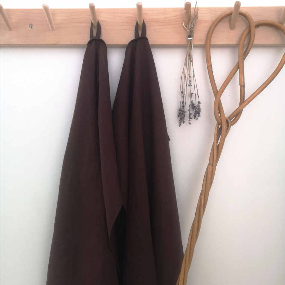bruna handdukar i linne hänger på träkrokar tillsammans med torkad lavendel och en äldre mattpiska.