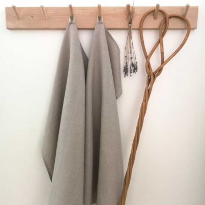 Naturligt ofärgade handdukar i linne hänger på träkrokar tillsammans med torkad lavendel och en äldre mattpiska.