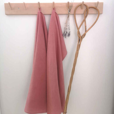 rosa handdukar i linne hänger på träkrokar tillsammans med torkad lavendel och en äldre mattpiska.