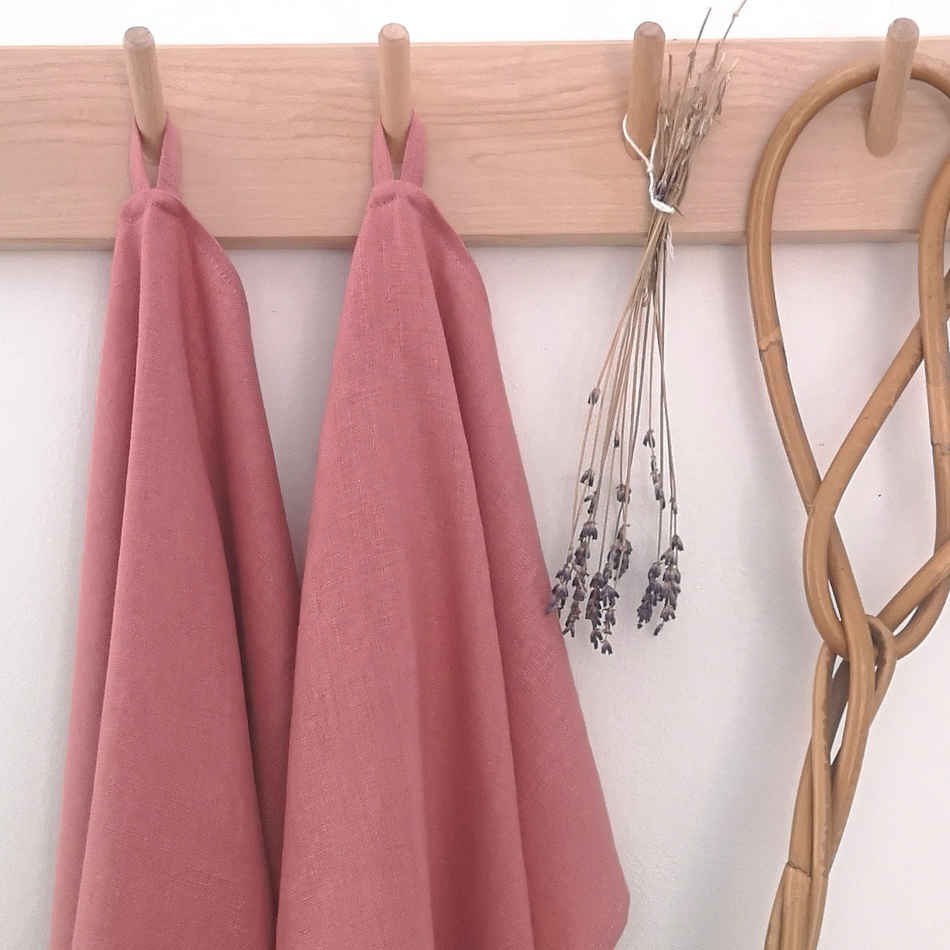 rosa handdukar i linne hänger på träkrokar tillsammans med torkad lavendel och en äldre mattpiska.