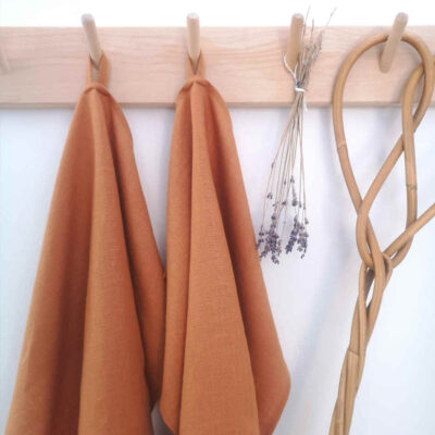 rostfärgade handdukar i linne hänger på träkrokar tillsammans med torkad lavendel och en äldre mattpiska.
