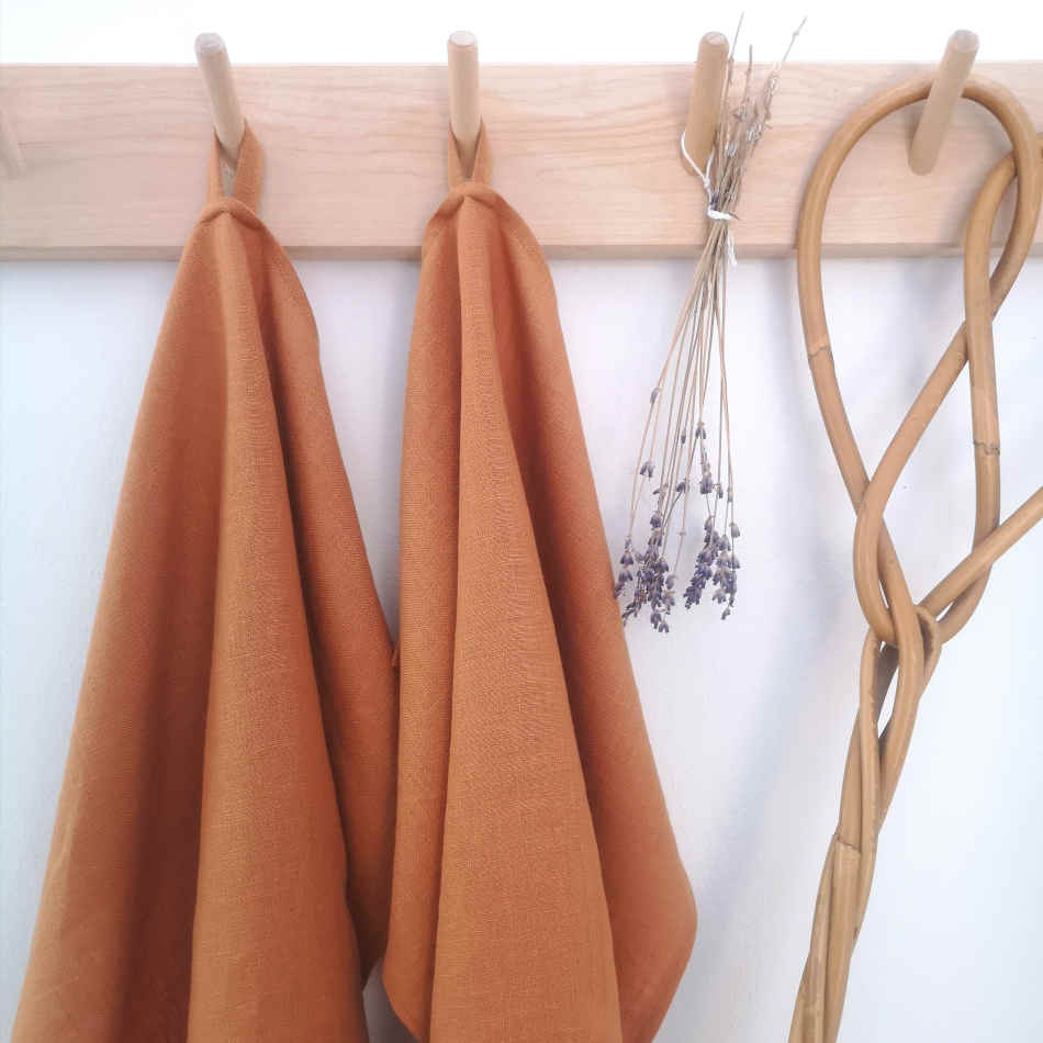 rostfärgade handdukar i linne hänger på träkrokar tillsammans med torkad lavendel och en äldre mattpiska.