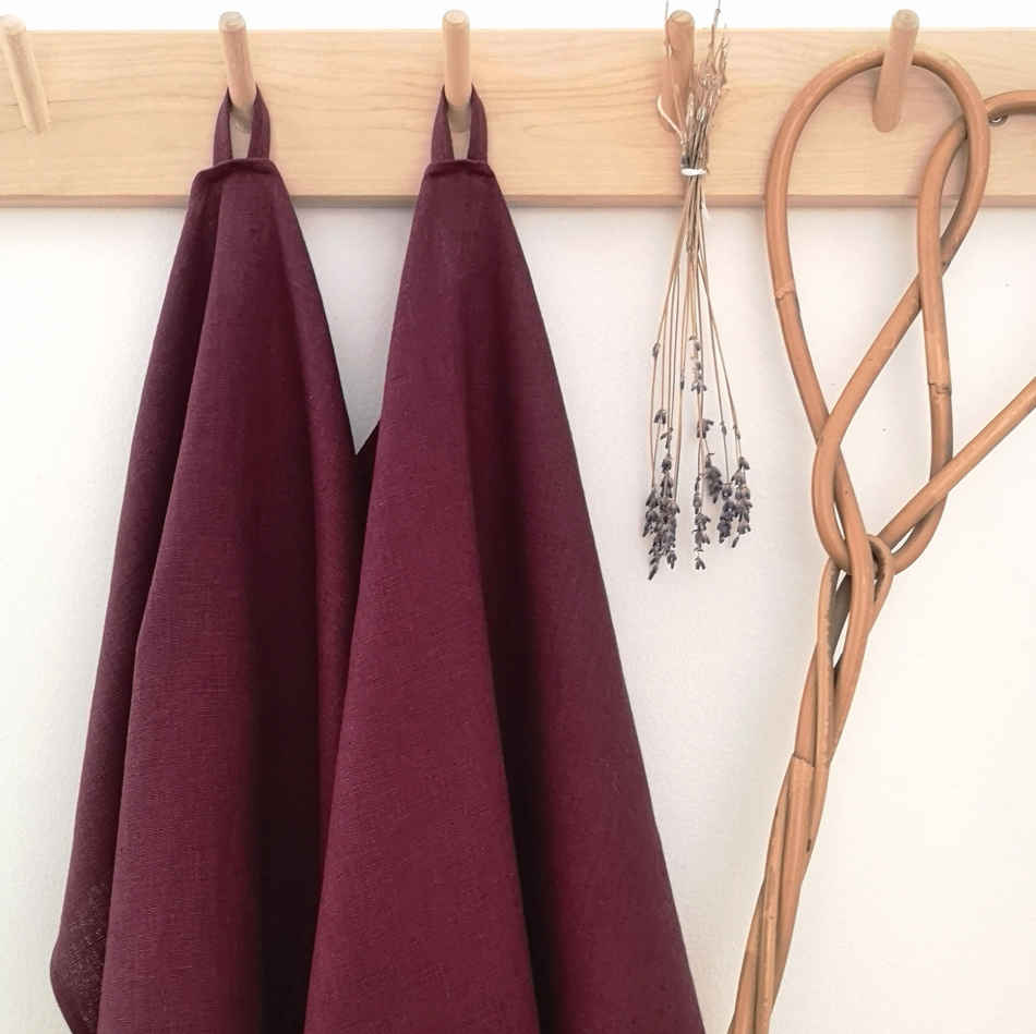 Vinröda handdukar i linne hänger på träkrokar tillsammans med torkad lavendel och en äldre mattpiska.