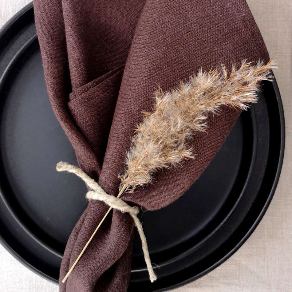 Brun servett vikt på svarta tallrikar på naturfärgad bordstablett.