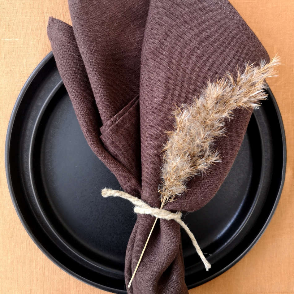 Brun servett vikt på svarta tallrikar på rostfärgad bordstablett.