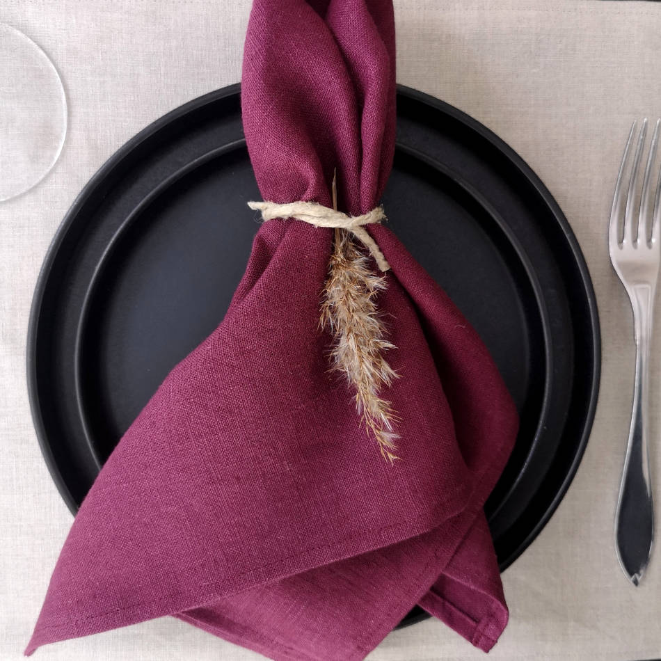 Vinröd linneservett på svarta tallrikar på naturfärgad bordstablett i linne.