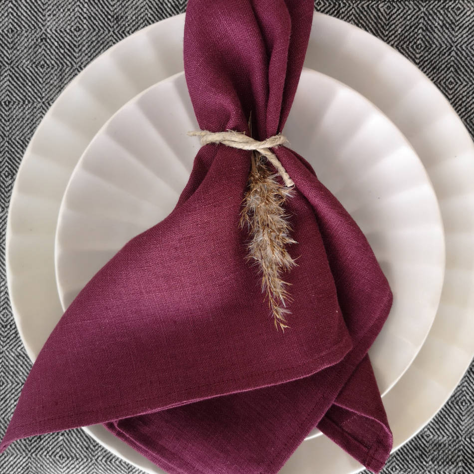 Vinröd linneservett vikt på tallrikar på en bordstablett med gåsöga-mönster