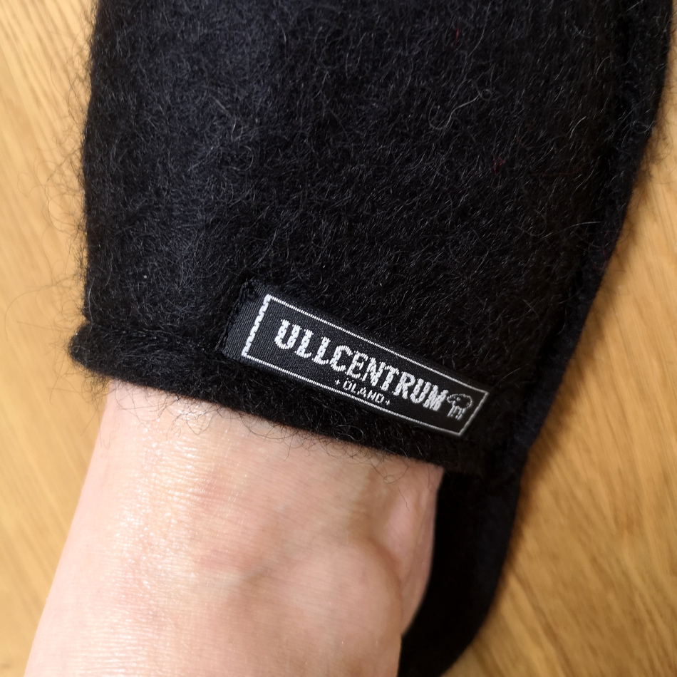 En svart tovad toffla i svensk ull med närbild på logotyp från Ullcentrum.