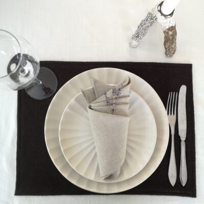 Mörkbrun bordstablett i återvunnen ull dukat med porslin och bestick samt naturfärgad servett.
