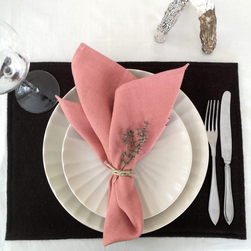 Mörkbrun bordstablett i återvunnen ull dukat med porslin och bestick samt rosa servett.