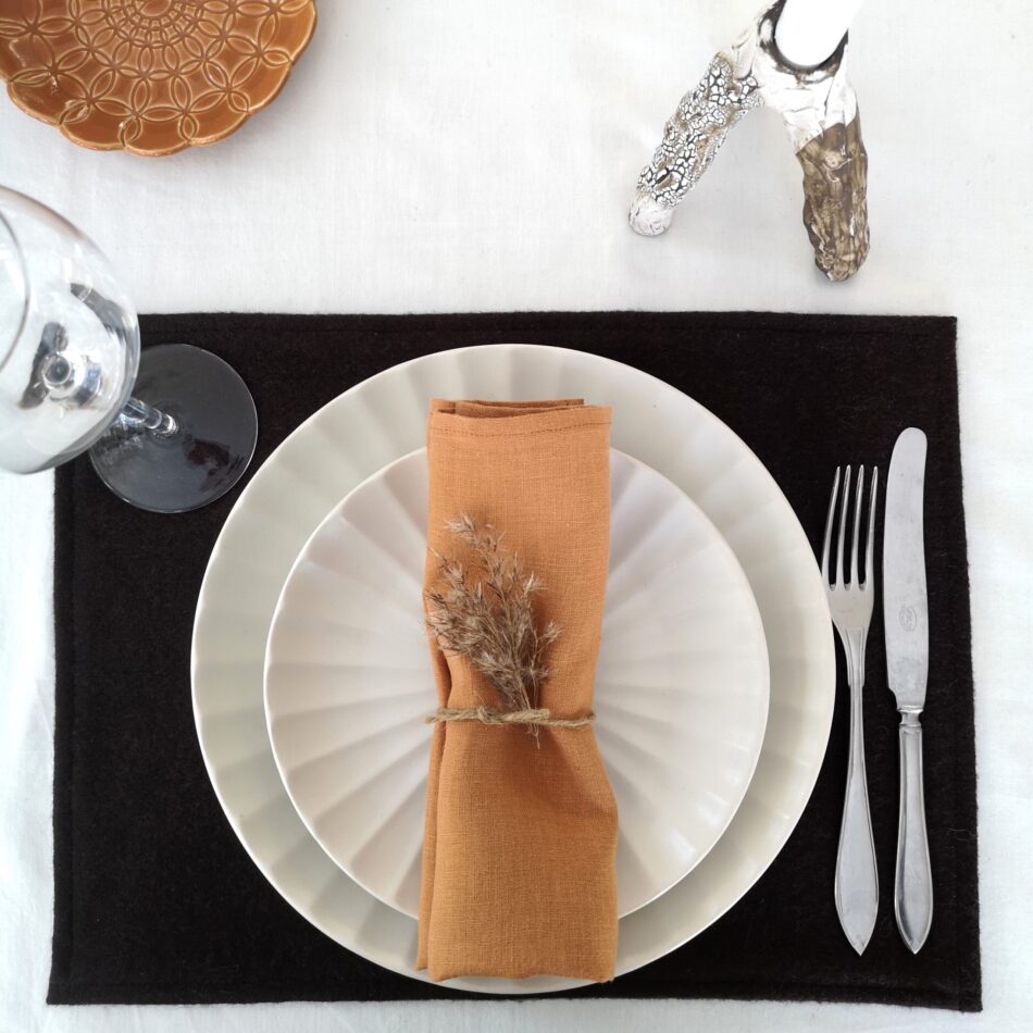 Mörkbrun bordstablett i återvunnen ull dukat med porslin och bestick samt rostfärgad servett.