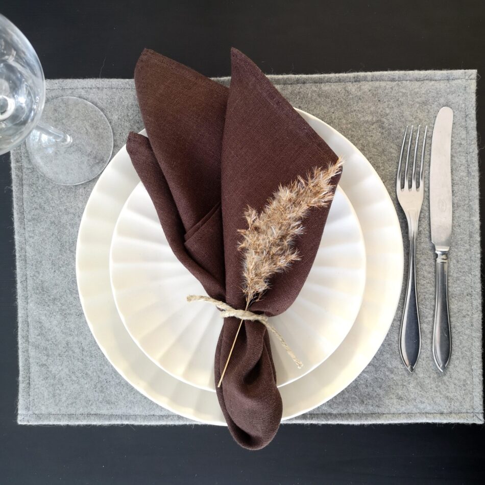 Ljusgrå bordstablett i återvunnen ull dukat med porslin och bestick samt brun linneservett.