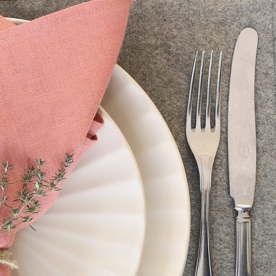 Ljusgrå bordstablett i återvunnen ull dukat med porslin och bestick samt rosa linneservett.