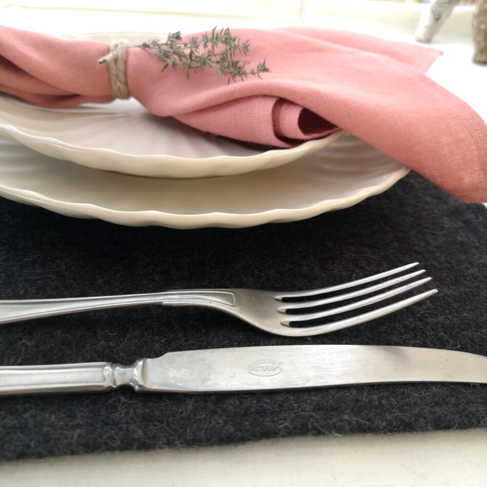 Mörkgrå bordstablett i återvunnen ull dukat med porslin och bestick samt rosa linneservett.