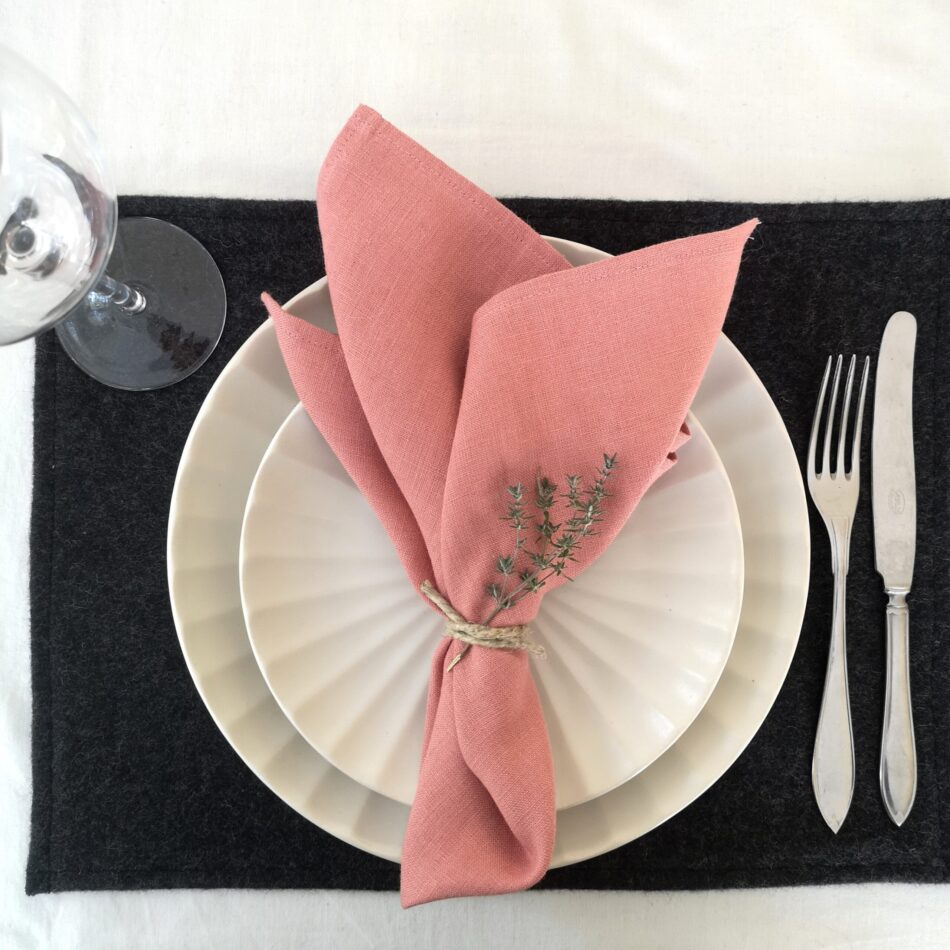 Mörkgrå bordstablett i återvunnen ull dukat med porslin och bestick samt rosa linneservett.