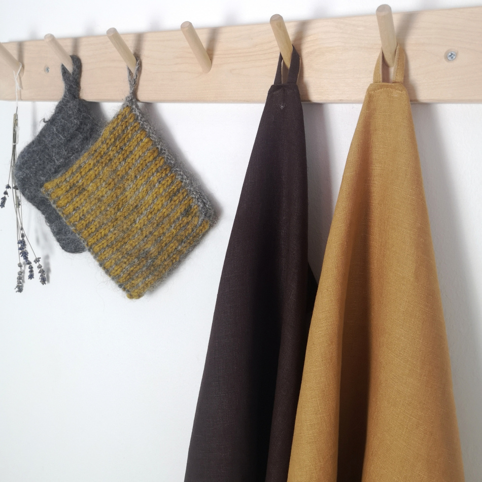 Brun och gula handdukar i ekologiskt linne på en trähängare tillsammans med grytlappar i ull.